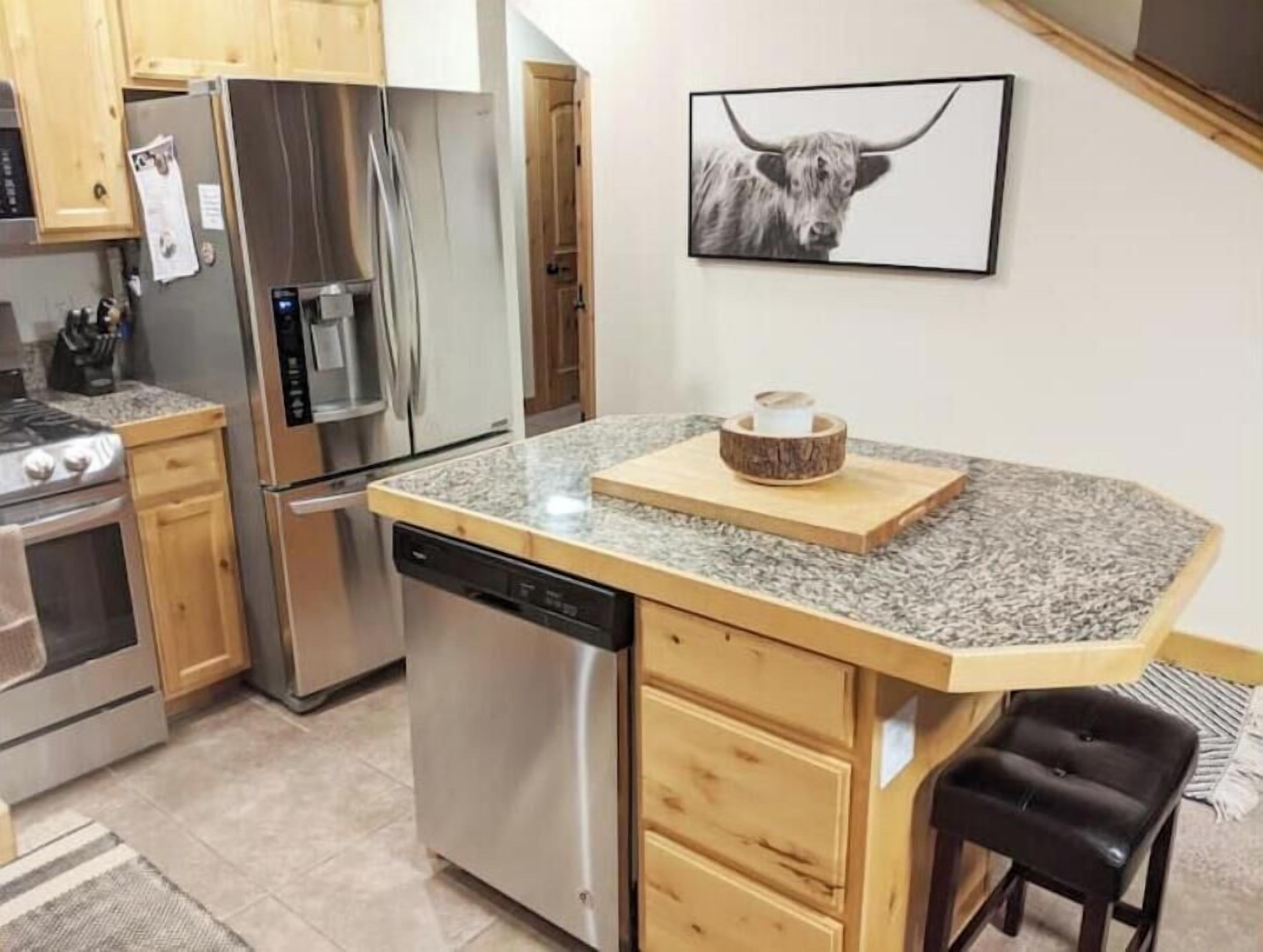 A kitchen with wooden cabinets, stainless steel appliances, a granite countertop, and a black leather stool.