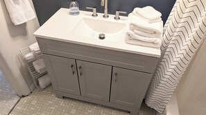 Un baño con un lavabo, tres grifos, un dispensador de jabón y un perchero para toallas.
