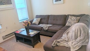 Un salon avec un canapé marron, une table basse et un tapis. Deux tableaux encadrés sont accrochés au mur.