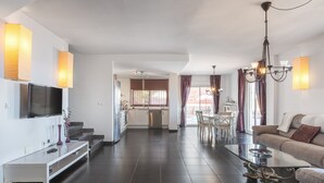 Un salon moderne doté d’un téléviseur à écran plat, d’une table basse en verre, d’un canapé et d’un coin repas avec une table et des chaises.