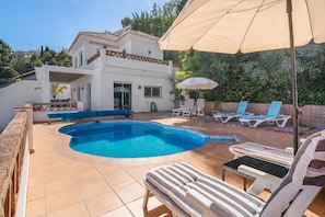 A swimming pool with lounge chairs and umbrellas, a white building with a tiled roof, and a brick wall. - Villa 'Romantica' with Sea View, Wi-Fi and Air Conditioning (Almuñécar)