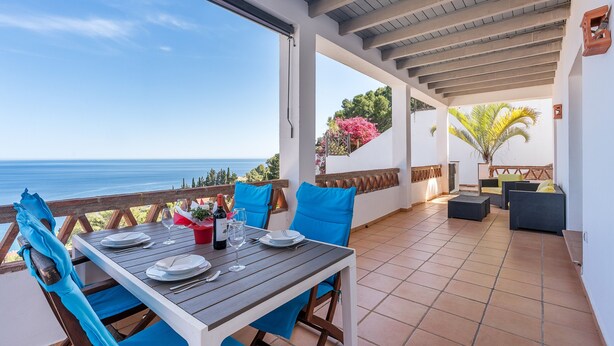 Une terrasse extérieure avec une table dressée pour le repas, des chaises et une vue sur la mer.