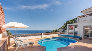 Une piscine sur le toit avec vue sur la mer, un parasol blanc et des chaises longues.