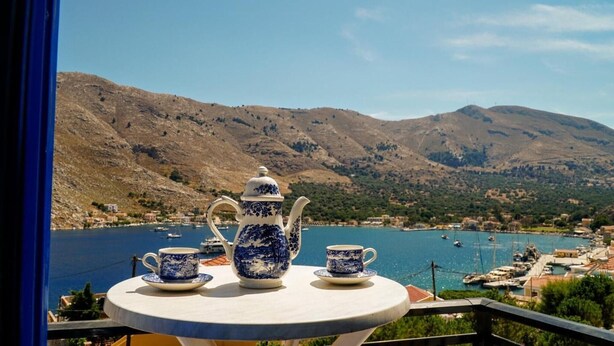A table with a teapot and cups, overlooking a bay with boats and a mountainous landscape. - Apartment 'Irene Family' with Sea View, Wi-Fi and Air Conditioning (Symi)