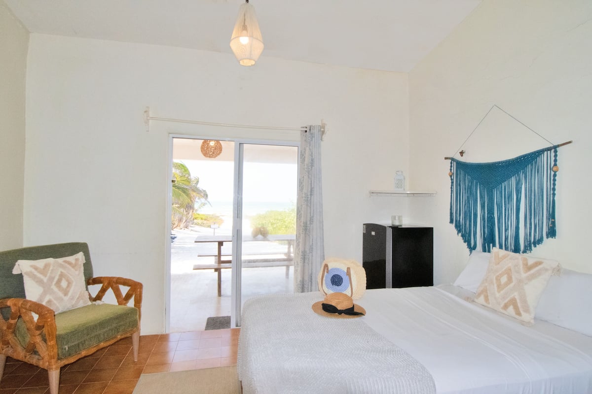 Une chambre avec un lit, une chaise, un bureau et une vue sur l’extérieur, visible à travers une porte vitrée.
