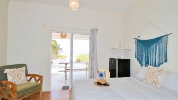 A bedroom with a bed, a chair, a desk, and a view through a glass door.