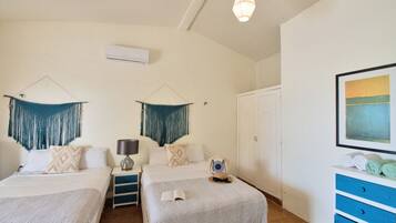 A hotel room with two beds, a wardrobe, a desk with a lamp, and a painting on the wall.