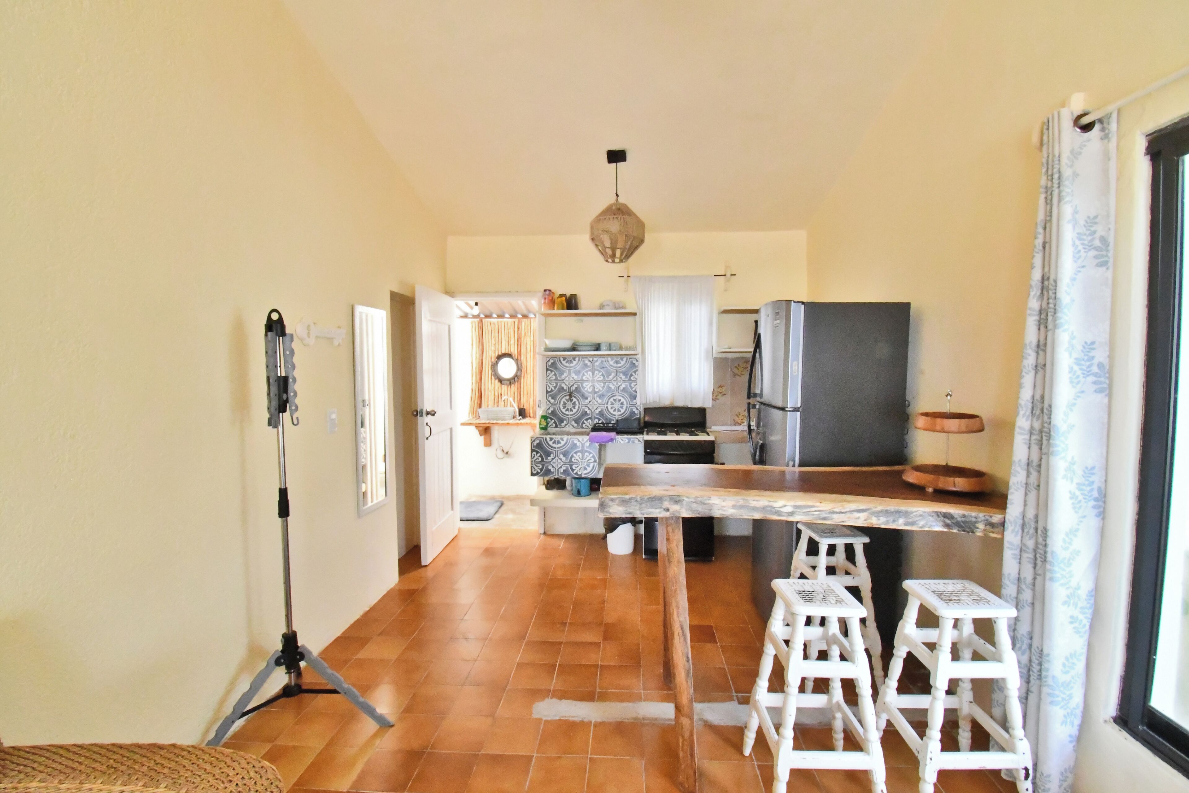 A kitchen with a wooden table, stools, a tripod, and a refrigerator.