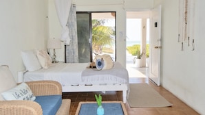 A bedroom with a bed, a nightstand, a lamp, a wicker chair, a blue cushion, and a view of the outdoors. - Arena y Mar Beachfront House, El Cuyo by The Spot Rentals (Tizimín)
