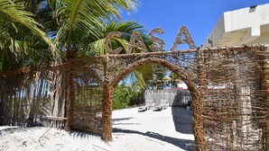 A beach entrance with a woven archway spelling "CASA" and a palm tree in the foreground. - Arena y Mar Beachfront House, El Cuyo by The Spot Rentals (Tizimín)
