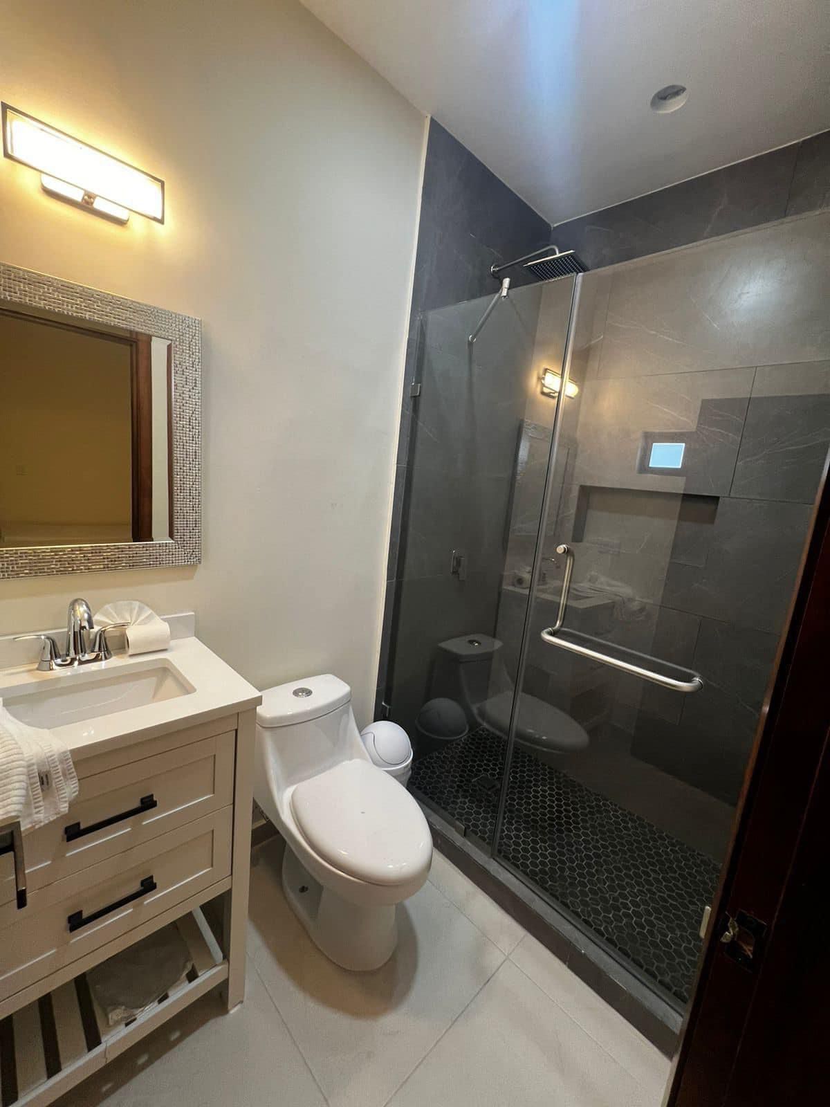 Un baño moderno con ducha envuelta en vidrio, un lavabo blanco y un mueble con cajones.