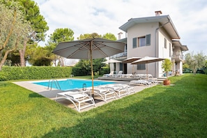 Una casa moderna con piscina, sillas de descanso y sombrillas.