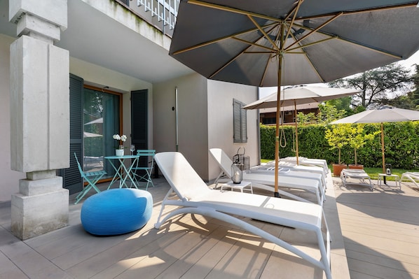 Un espacio lounge exterior moderno con sillones blancos, un sillón tipo saco y sombrillas.