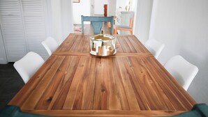 Una mesa de comedor de madera con sillas, un cojín color turquesa y un objeto metálico sobre la mesa.