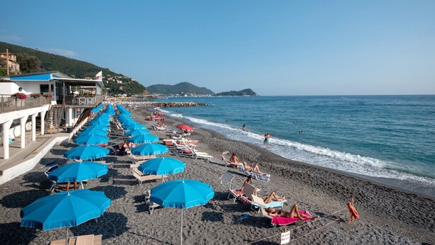 A beach with rows of blue umbrellas, beach chairs, and a building with a blue roof. - Apartment 'Lulu' with Private Terrace, Wi-Fi, Convenient for Cinque Terre and Portofino (Lavagna)