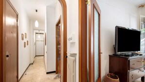 A hallway with a radiator, a wooden door, a television on a dresser, and a woven bag on the floor. - Apartment 'Lulu' with Private Terrace, Wi-Fi, Convenient for Cinque Terre and Portofino (Lavagna)