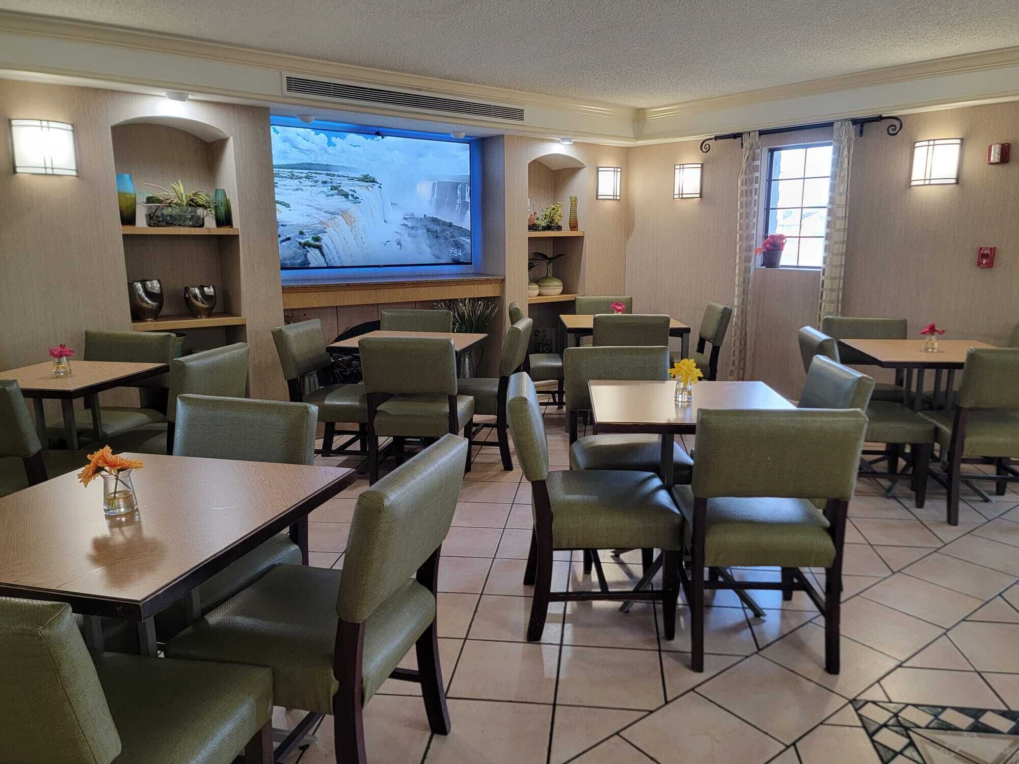 Un restaurant doté de nombreuses tables et chaises, d’un grand écran diffusant une vidéo de cascades et d’étagères ornées d’objets décoratifs.