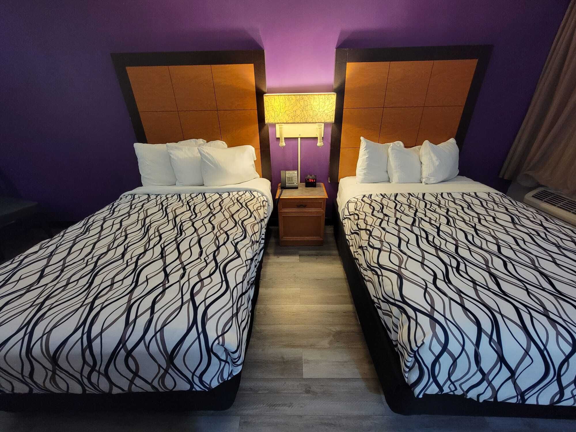 A hotel room with two beds, each with a patterned bedspread, a nightstand with a lamp, and a wooden headboard.