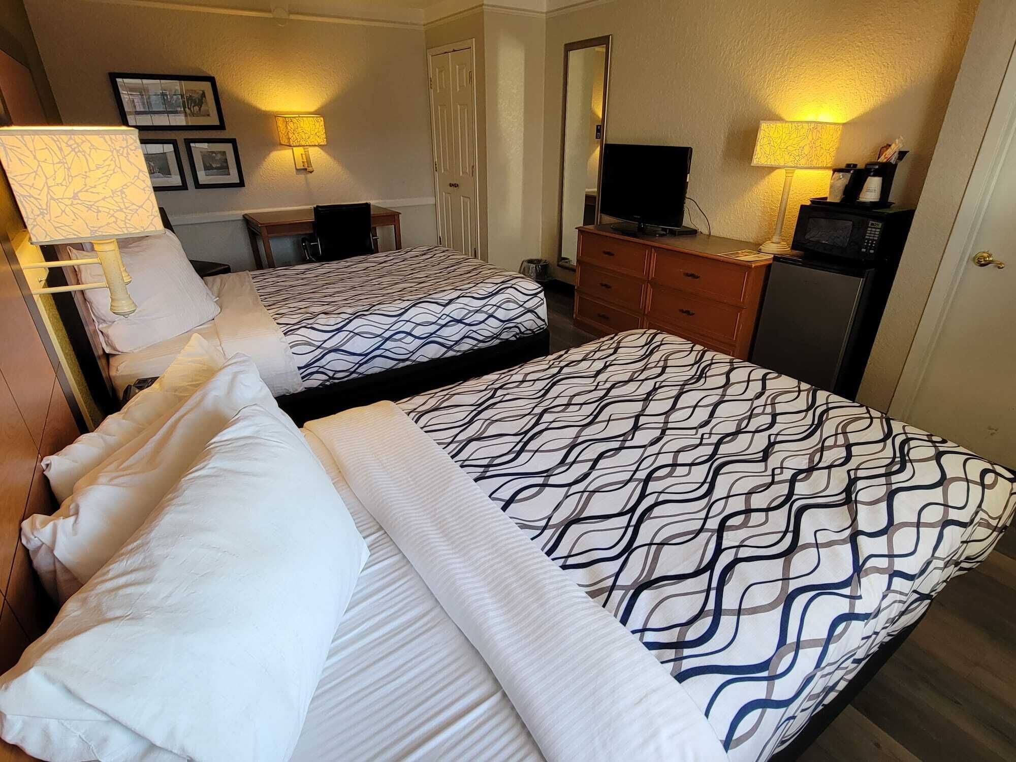 Ein Hotelzimmer mit zwei Betten, einem Schreibtisch, einem Fernseher, einem Schminktisch und Wandlampen.