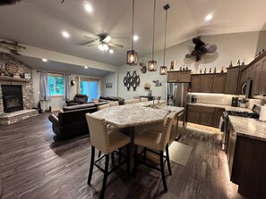 A spacious living area with a fireplace, leather sofa, and a dining table with chairs. - Cabin in the Woods-Sleeps 10! (Iola)
