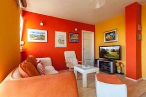 Relax in this stylish living room with a vibrant color scheme, featuring three framed artworks, a TV, and a cozy table with a vase of flowers.