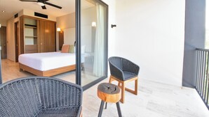 A modern bedroom with a large bed, a ceiling fan, and a glass door leading to a balcony with wicker chairs and a wooden stool. - Hacienda Tuk by The Spot Rentals (Tulum)