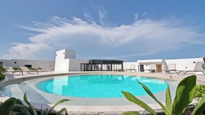 A pool area with lounge chairs and a building with large windows. - Hacienda Tuk by The Spot Rentals (Tulum)
