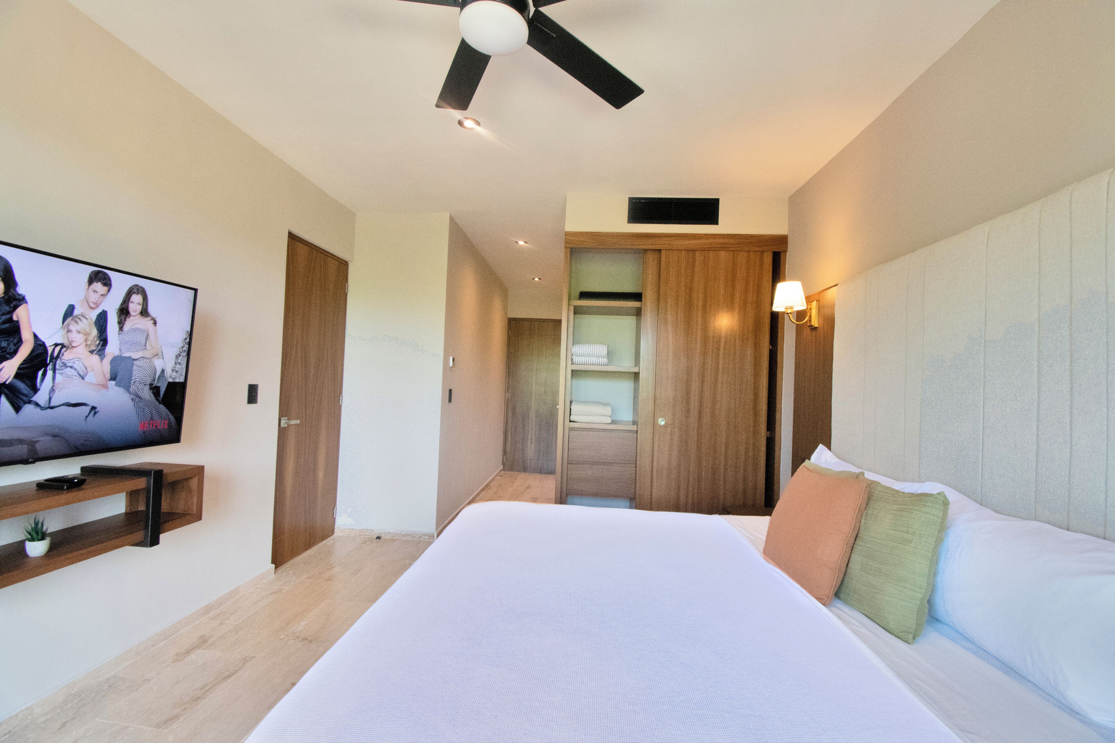 A hotel room with a large bed, a ceiling fan, a TV on a stand, and a walk-in closet.