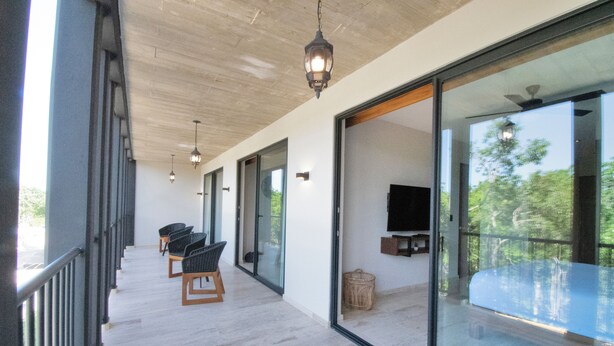 A modern interior with a long corridor, glass doors leading to a balcony, and a flat-screen TV mounted on the wall. - Hacienda Tuk by The Spot Rentals (Tulum)