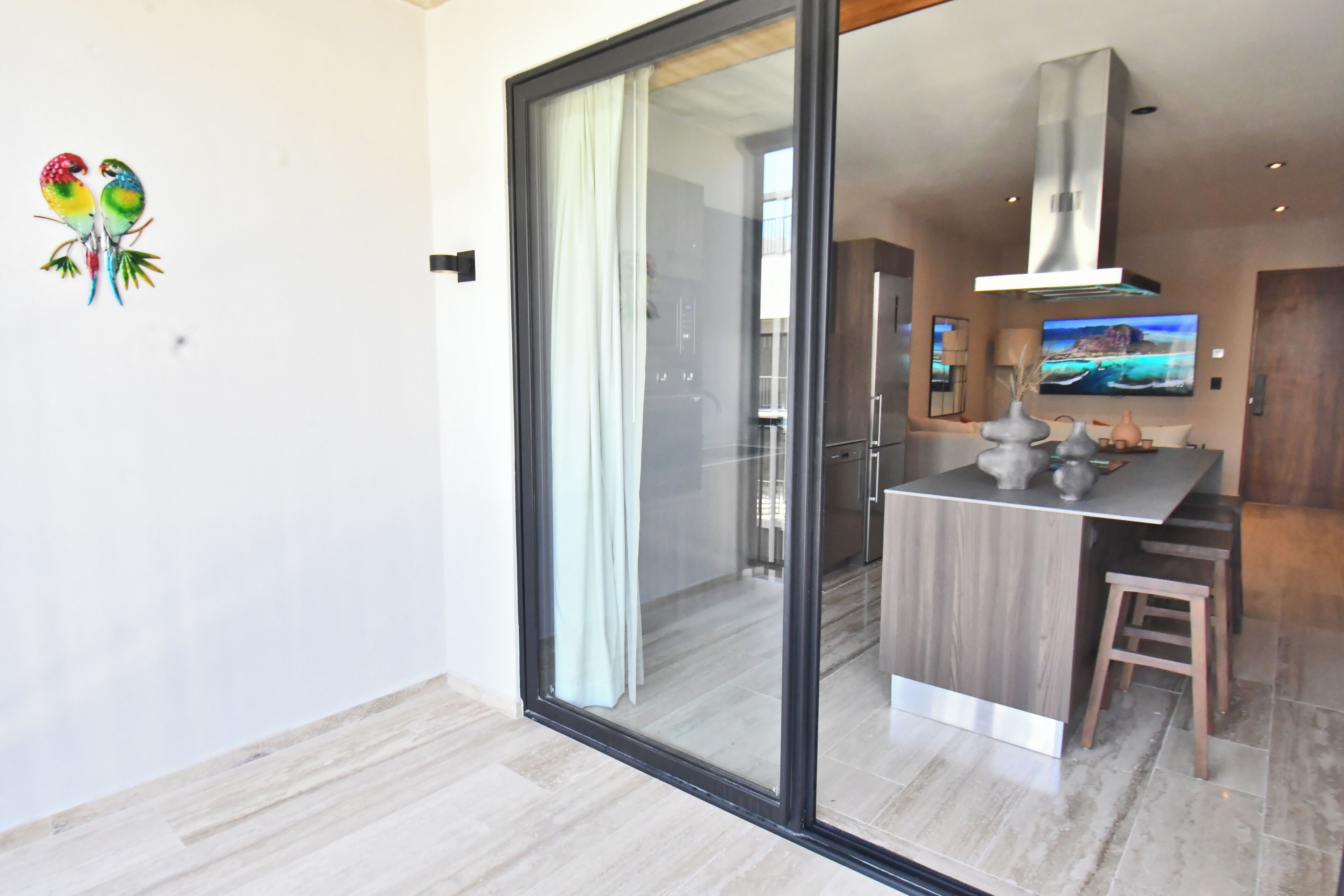A modern kitchen with a large island, a sliding glass door, and a dining area with a wooden stool.