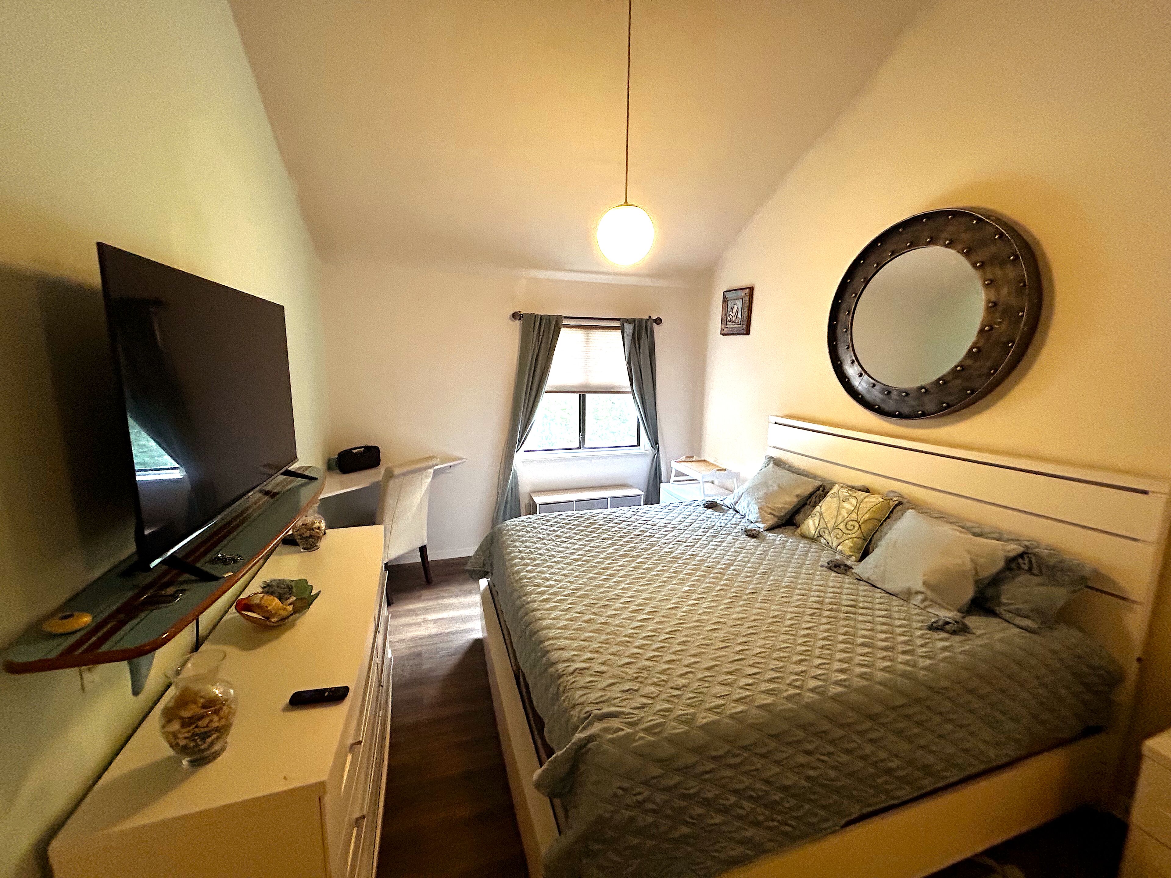 A bedroom with a bed, a TV, a desk, and a mirror.