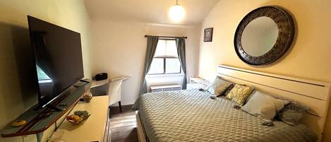 A bedroom with a bed, a TV, a desk, and a mirror.