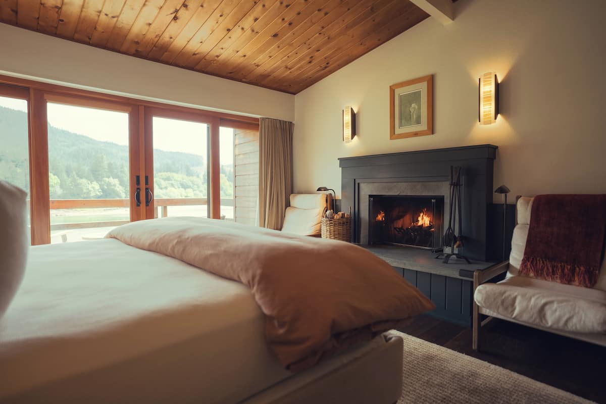 Un dormitorio con cama, chimenea, vistas al exterior y una ventana con cortinas.