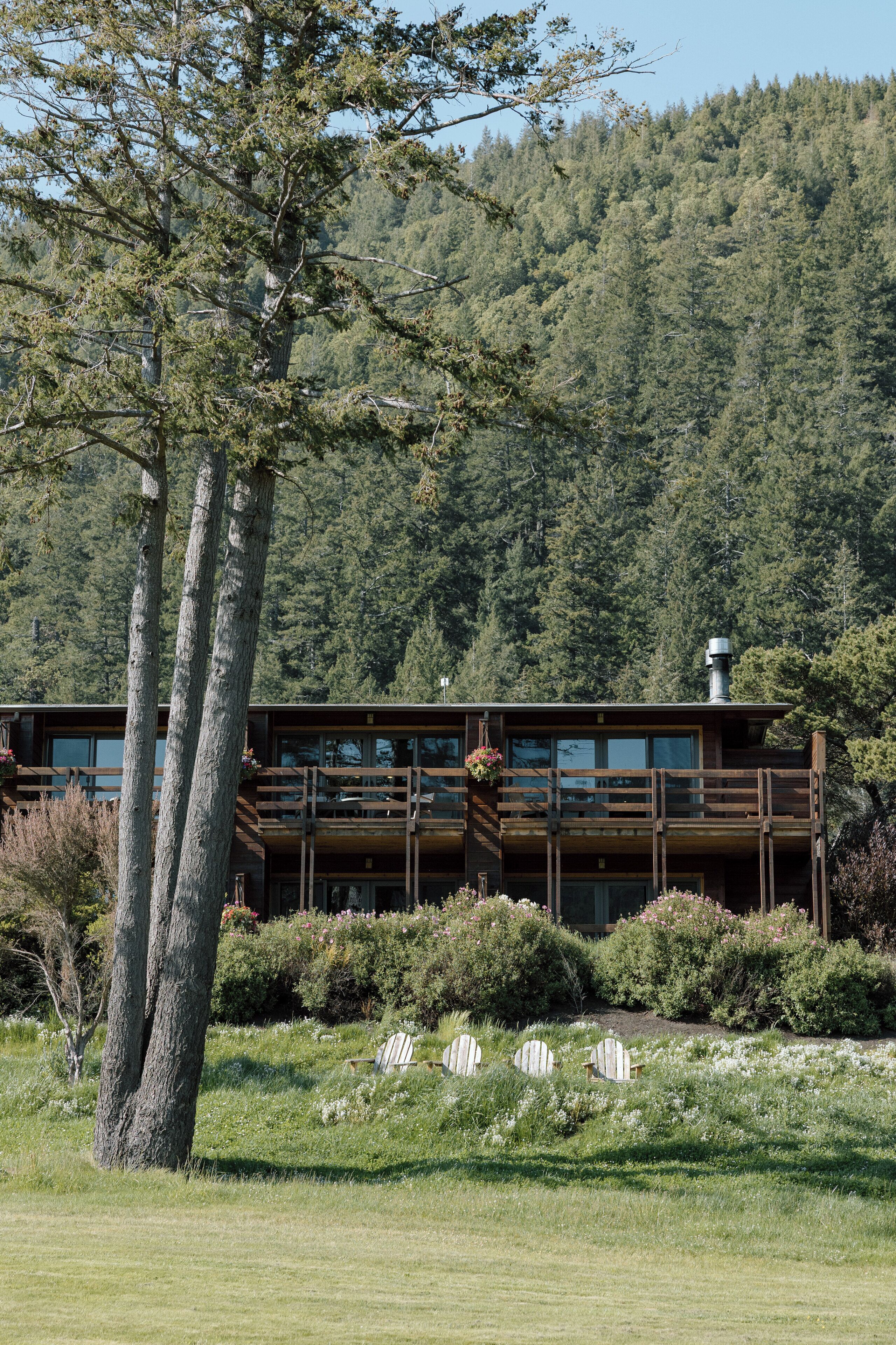 A cabin with a wooden deck, surrounded by a forested hillside.