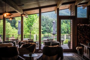 Un intérieur chaleureux avec des poutres en bois, de grandes fenêtres et un espace extérieur aménagé pour s’asseoir.