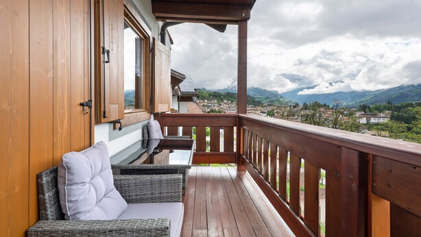 Un balcón de madera con mobiliario de mimbre y vistas a un pueblo y montañas.