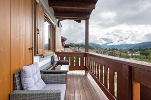 A wooden balcony with wicker furniture and a view of a town and mountains. - Apartment 'Casa Elisabeth' with Mountain View, Shared Garden and Balcony (Cavalese)