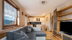Un interior moderno con sofá, televisión, cocina y vistas a través de una ventana.