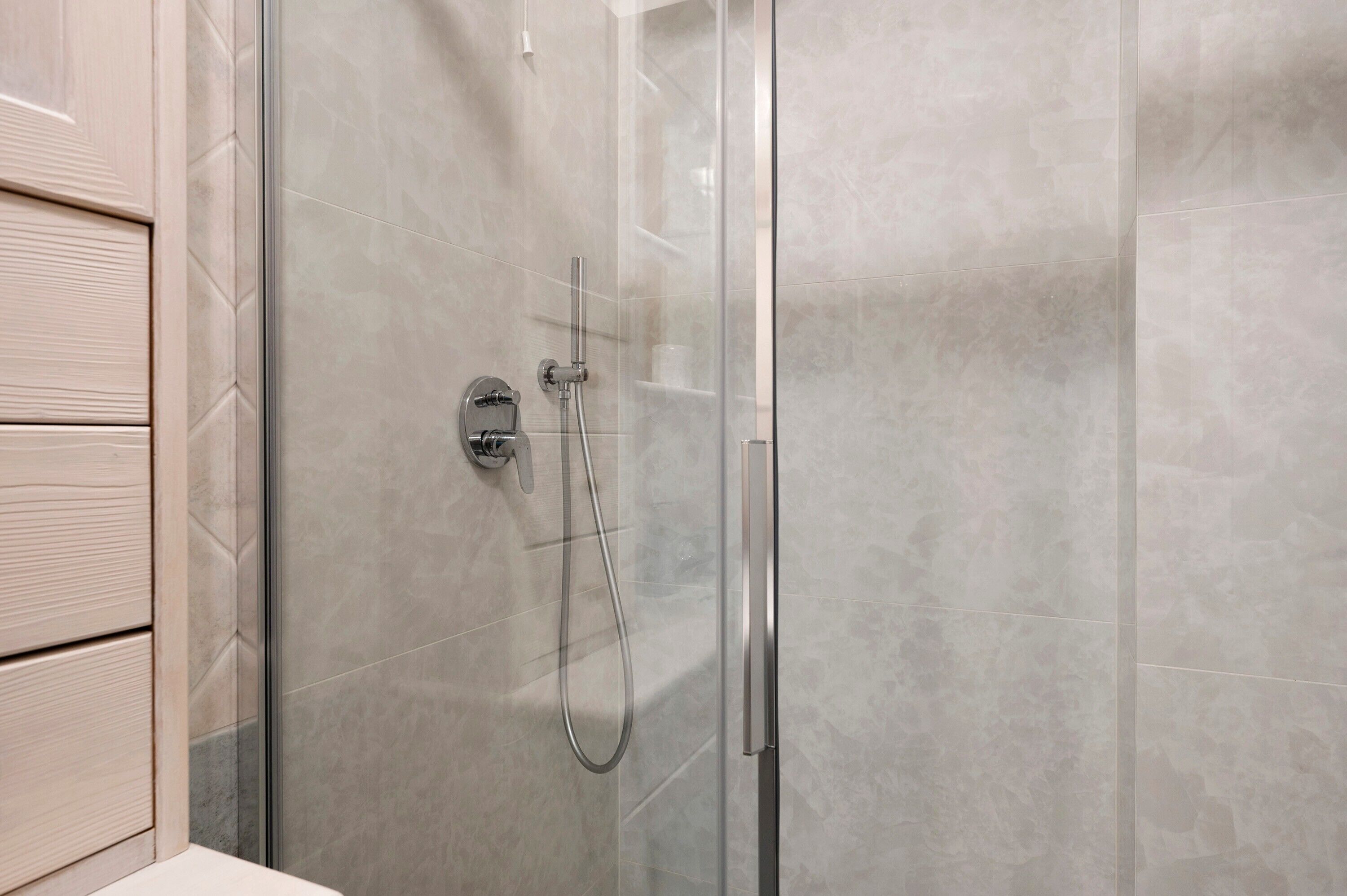 Une douche fermée par des parois en verre, dotée d’un pommeau de douche à main et d’un panneau de commande fixé au mur.