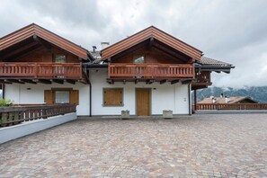 A two-story building with a wooden balcony, a tiled roof, and a paved courtyard. - Apartment 'Casa Elisabeth' with Mountain View, Shared Garden and Balcony (Cavalese)
