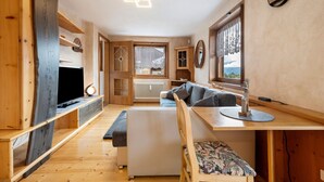 Un interior moderno con un mueble de televisión de madera, un sofá, una mesa de comedor y una ventana con vistas.