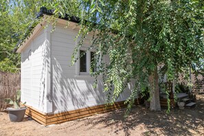 Une petite cabane en bois, d’un seul étage, avec une fenêtre, entourée d’arbres et située sur un sol en terre.