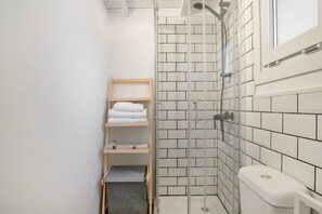 Et badeværelse med brusebad, toilet og en hylde med håndklæder.