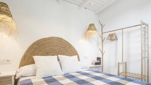 Una cama con colcha de cuadros, cabecero tejido y dos lámparas colgantes.
