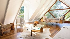 Amplio dormitorio tipo loft con tragaluces grandes, una hamaca colgante y una mesa de centro de vidrio.