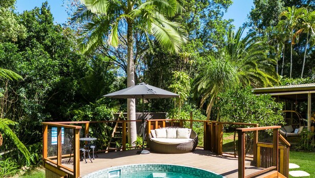 Una bañera de hidromasaje circular rodeada por una terraza de madera, con una zona de estar con cojines y una sombrilla.