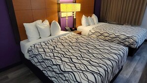 A hotel room with two beds, a headboard, a nightstand, a lamp, and a curtain.