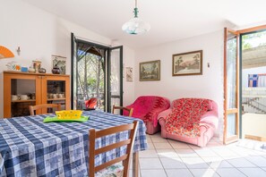 A dining area with a table set for two, a pink sofa, and a wooden cabinet with dishes. - Holiday Home 'Su Entu A Mari Museddu' with Sea View, Shared Garden and Wi-Fi (Cardedu)