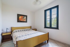 A bedroom with a bed, a nightstand, a lamp, a framed picture, and a window. - Holiday Home 'Su Entu A Mari Museddu' with Sea View, Shared Garden and Wi-Fi (Cardedu)