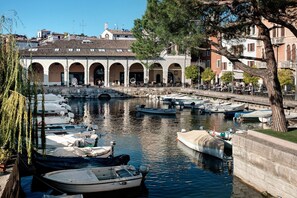 A canal with boats docked, a stone building with arches, and a tree in the foreground.